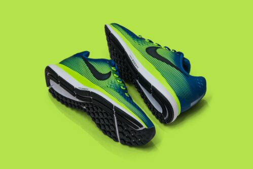 From above of colored sneakers with blue and green surface and green and white and black sole for comfortable moving around streets against green background